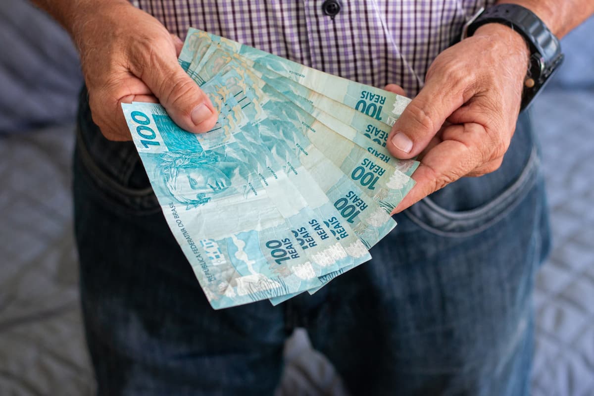 Homem segurando notas de 100 reais
