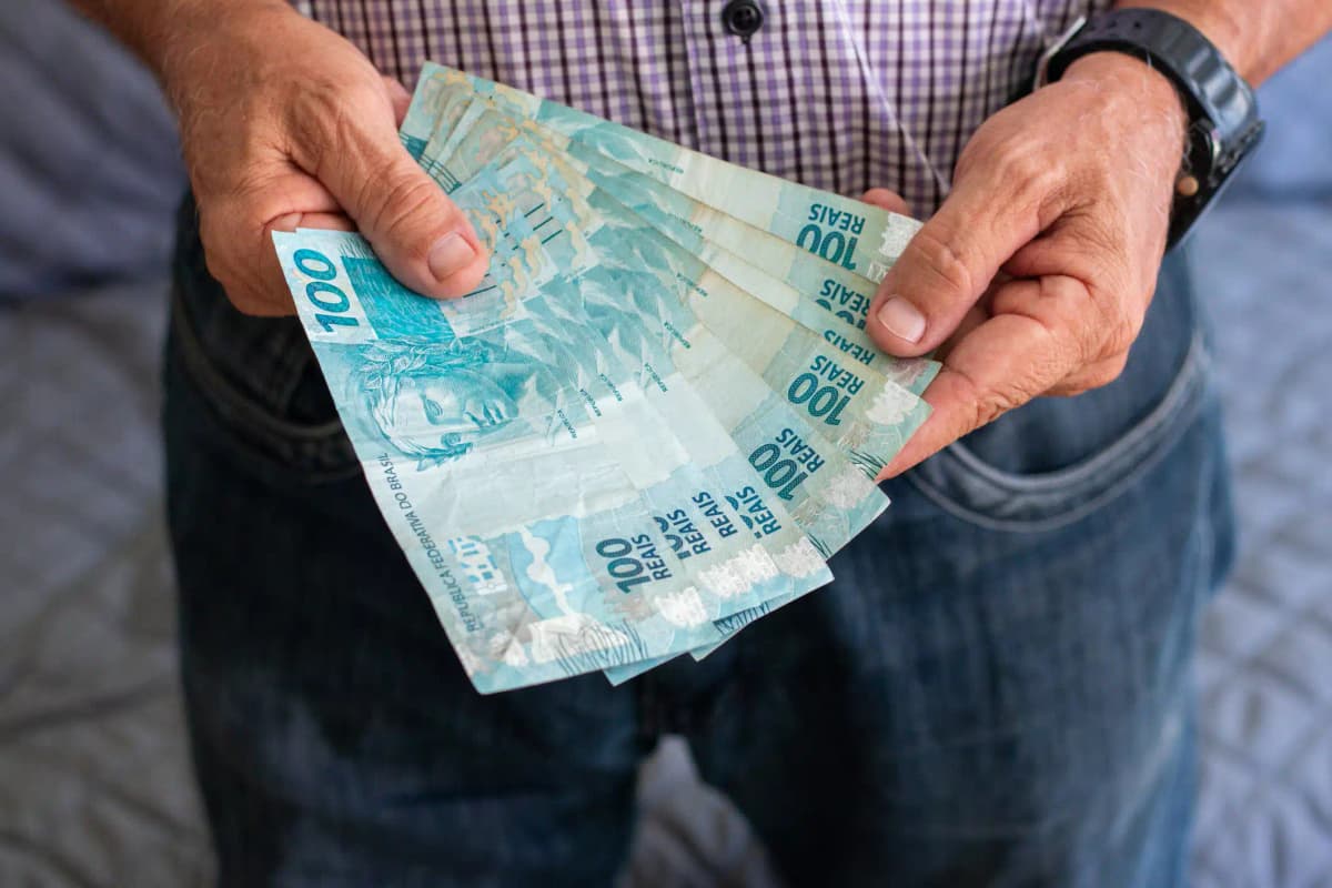 Homem segurando notas de 100 reais