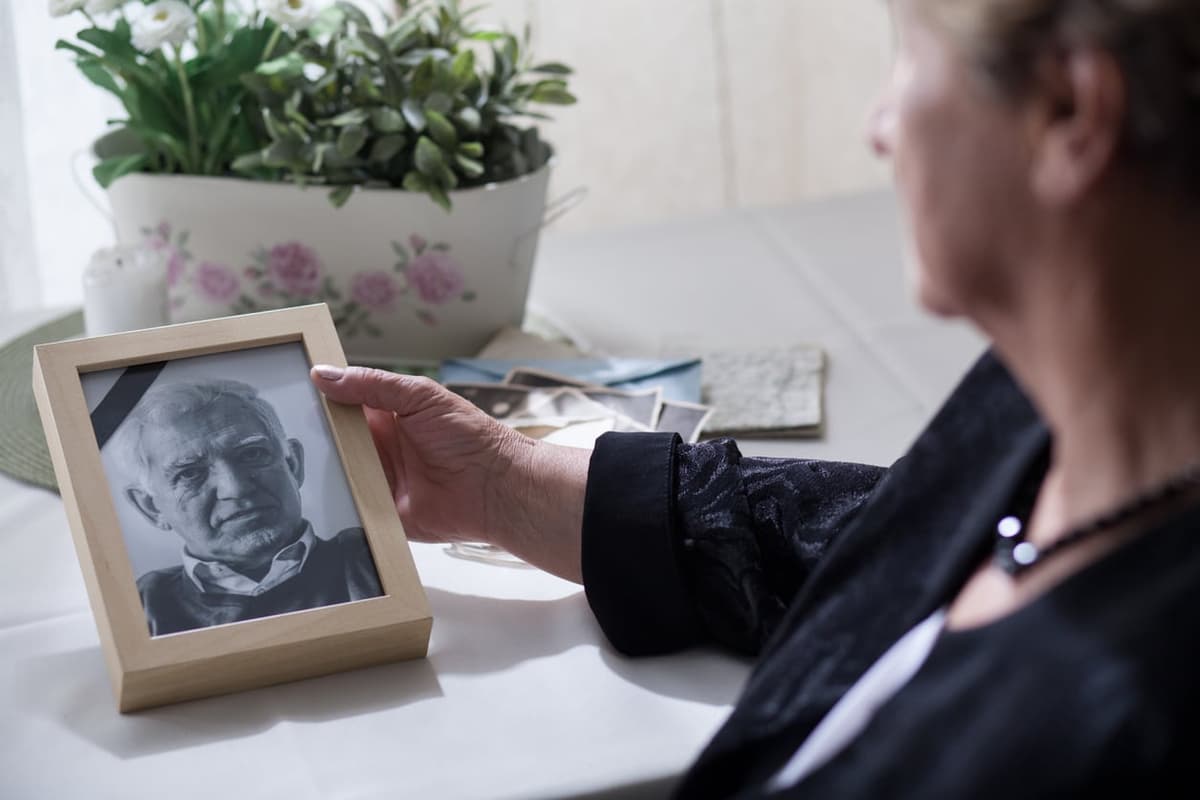 mulher idosa olhando para porta retrato de marido falecido