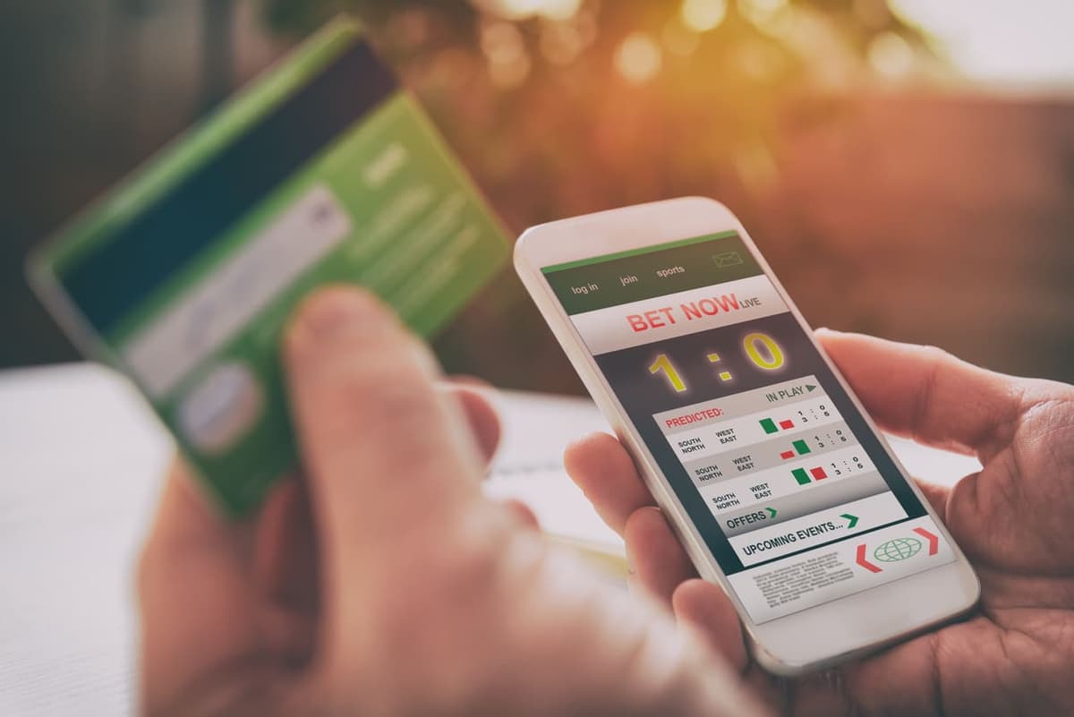 mão de homem, em destaque segurando celular com bet e em outra mão cartão