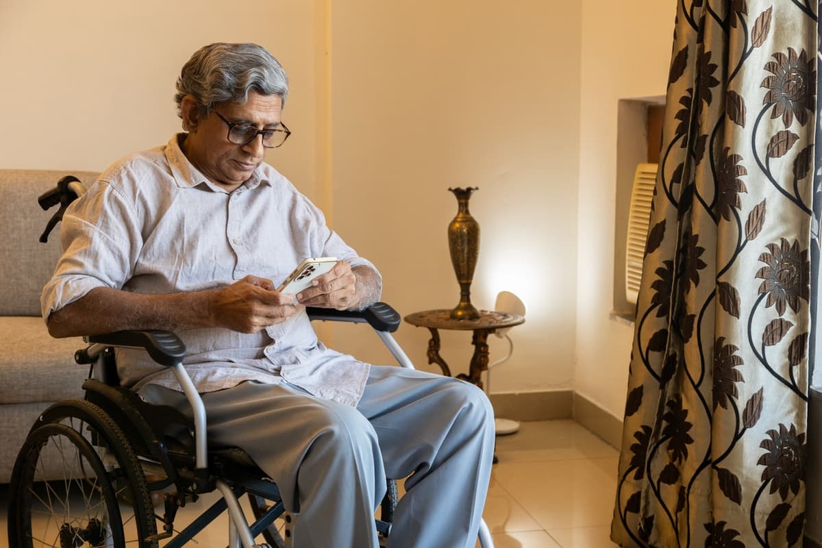 Homem com deficiência usando smartphone sentado em cadeira de rodas em casa