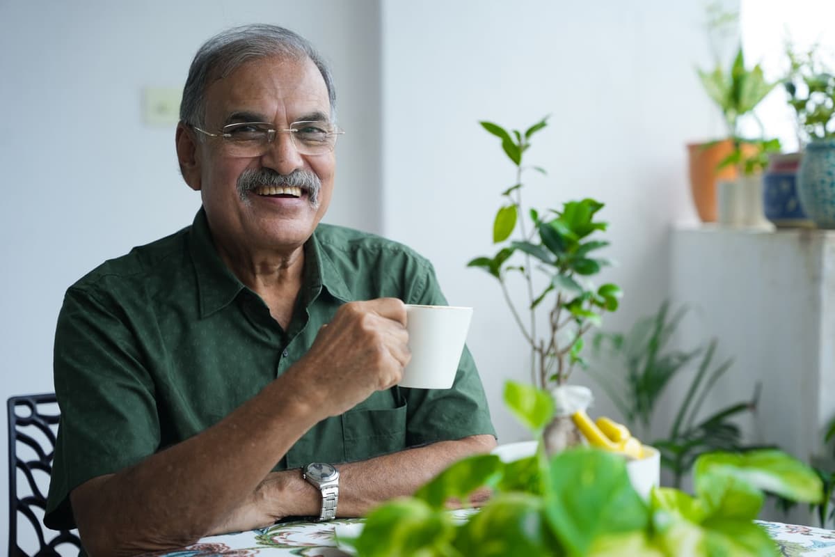homem idoso sorrindo, sentado próximo a mesa segurando uma caneca